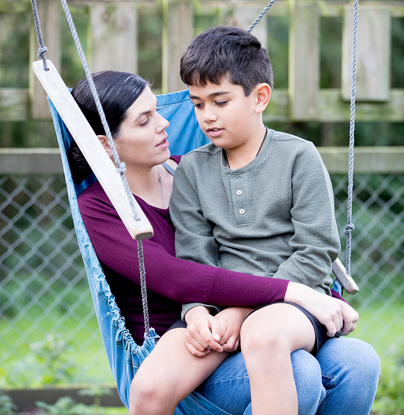A mother sitting and talking on a homemade swing with her son in her lap.